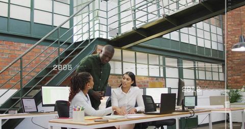 Diverse team collaborating, reviewing documents around laptop in modern industrial loft office