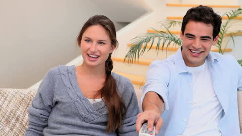 Couple Relaxing on Couch Watching Television and Laughing