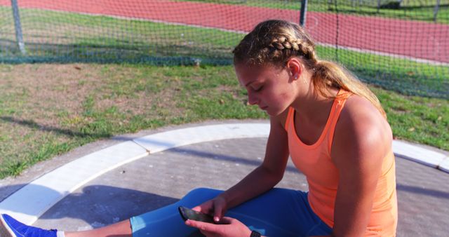 Young Female Athlete Sitting on Track Checking Her Smartphone Outdoors - Download Free Stock Images Pikwizard.com