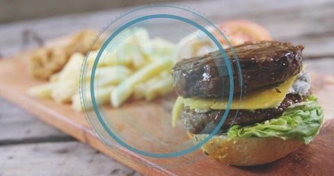 Double-patty cheddar burger on rustic wooden board with fries and circular blue overlay