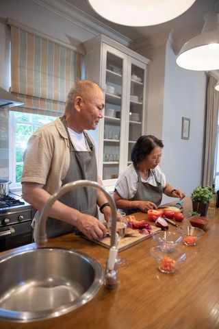 Asian couple cooking together at home kitchen island chopping tomatoes and onions