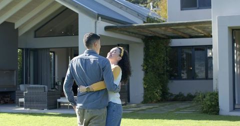 Diverse couple hugging in front of modern home