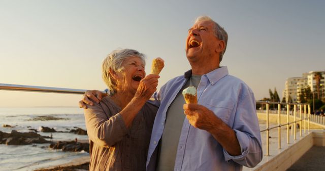 Happy senior caucasian couple eating ice cream and embracing by sea. Retirement, relationship, love, togetherness, free time, food and drink and relaxing, unaltered.