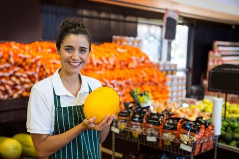 Smiling Female Grocer Holding Fresh Melon in Produce Section