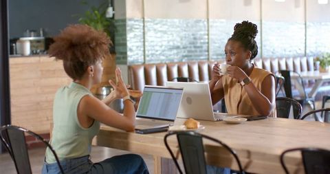 Two african american women collaborating over laptops in modern cafe