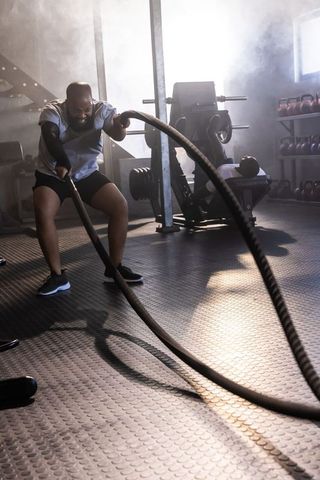 African american men training pulling heavy battle ropes in gym with hazy backlight