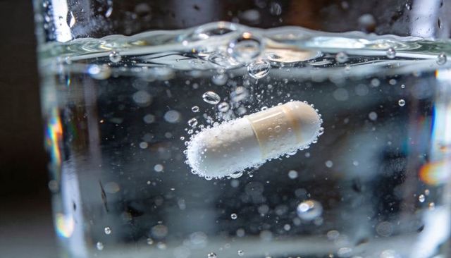 Effervescent white capsule dissolving and releasing bubbles in glass of water, macro closeup