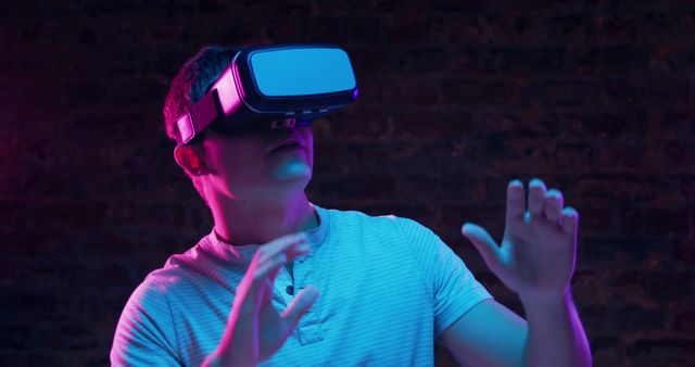 Young Caucasian man explores virtual reality in a neon-lit room. His gestures suggest immersion in a cutting-edge VR experience at home.