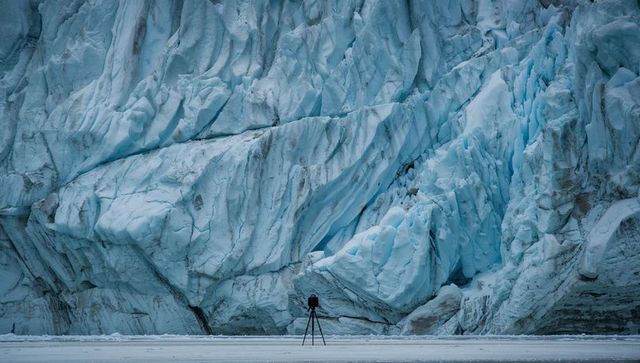 Lone photographer capturing towering blue glacier wall with crevasses and jagged seracs