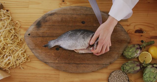 Hands of caucasian female cook slicing fish on cutting board in kitchen. Lifestyle, food, cooking and senior lifestyle, unaltered.