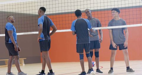 Diverse young male volleyball players talking at net in indoor gymnasium team huddle