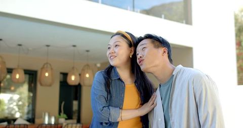 Young diverse couple admiring modern home from sunlit patio, sharing joyful moment