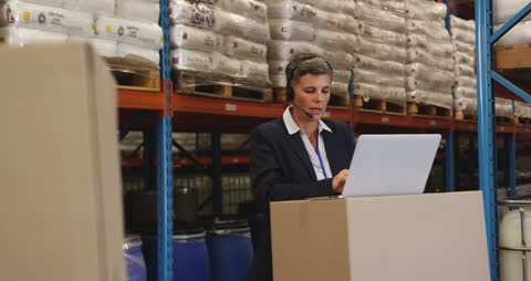 Warehouse Manager Using Laptop with Headset in Distribution Center