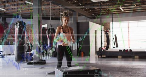 Female athlete checking watch at plyo box in industrial gym with financial data overlay