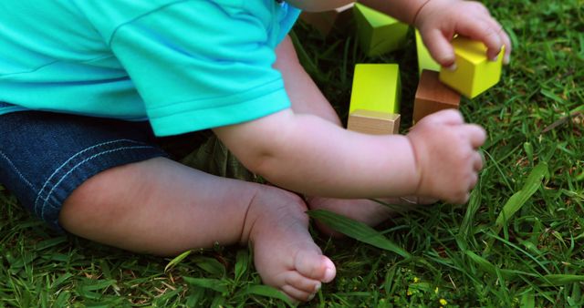 Adorable baby sitting on grass, exploring and playing with colorful blocks. Ideal for use in promotions related to childhood development, early learning, outdoor activities, parenthood, or childcare products.