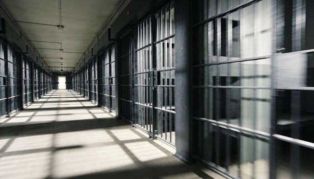 Empty deserted prison cellblock corridor leading toward bright exit casting bar shadows