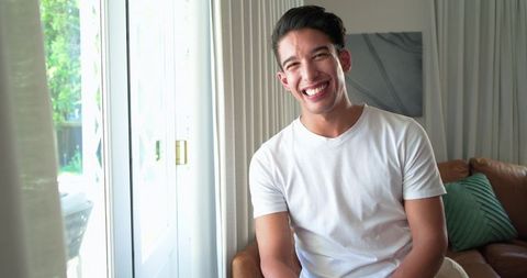 Happy african american man smiling on sofa by sunlit sliding door in cozy living room