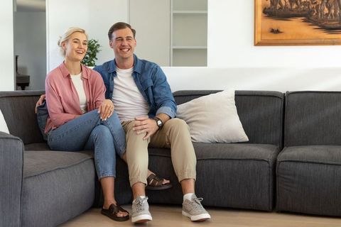 Happy couple relaxing on modern gray sectional sofa in bright minimal living room smiling