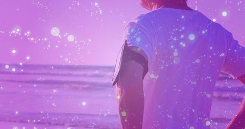 Senior man wearing phone armband watching lavender dusk over ocean horizon with bokeh