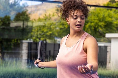 Young african american woman playing pickleball on sunlit backyard court in pink tank top
