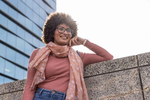 Smiling african american woman leaning on urban wall wearing polka-dot scarf and glasses