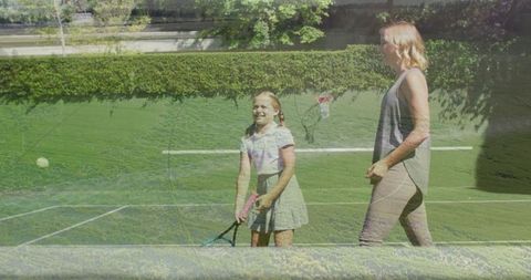 Mother coaching daughter on outdoor tennis court