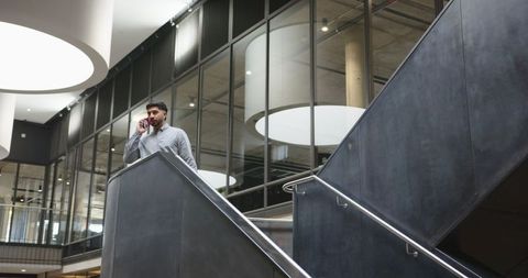 Professional Man on Smartphone in Modern Office Atrium by Staircase