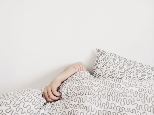 Person resting in bed with patterned white and black bedding. Ideal for concepts of relaxation, comfort, and modern home living. Can be used in blog posts on sleep, bedroom designs, or advertisements for home goods.