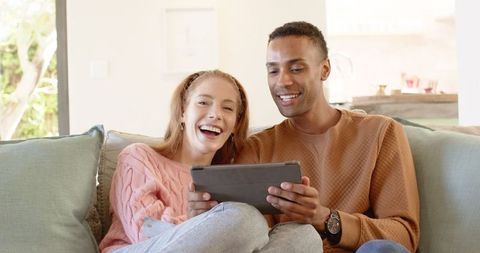 Joyful couple using tablet on cozy sofa in bright living room