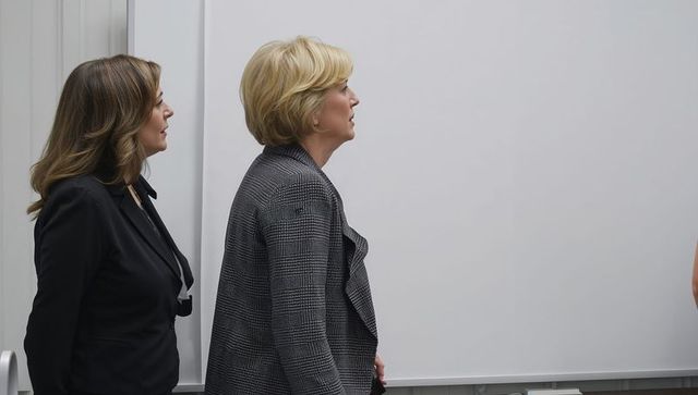 Two professional women standing beside whiteboard in office, business colleagues profile