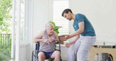 Caregiver Teaching Senior Tablet Use in Sunlit Home With Wheelchair and Green Balcony View