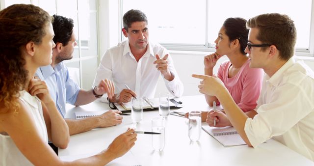 Group of five professionals engaged in a serious business meeting, sitting around a table in a modern office. Ideal for visual content on corporate communications, leadership, teamwork, decision-making, and business strategy. Useful for websites, presentations, and marketing materials related to business and professional environments.