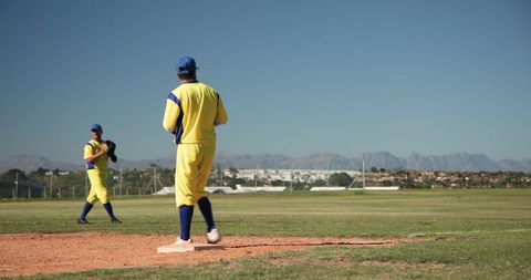 Baseball Teammates Standing on Base in Yellow Uniforms with Mountain Background, Sunny Day