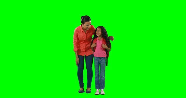 Mother and daughter sharing a loving moment while standing on green background. They are both smiling and the mother has her arm around the child. The child is wearing a backpack, suggesting a school context. This can be used for advertising family products, educational content, parenting blogs, or school campaigns.