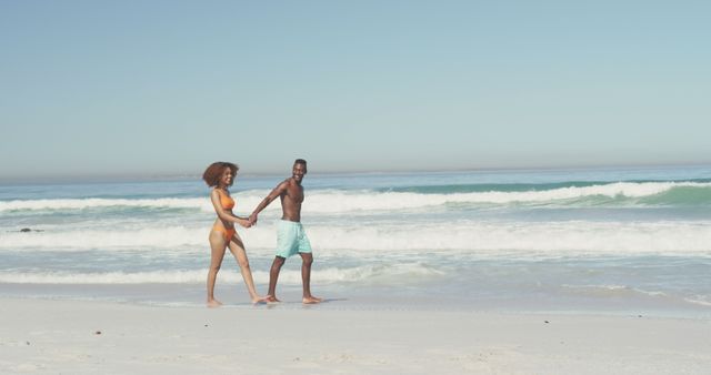 Happy diverse couple holding hands and walking on sunny beach by the sea. Summer, relaxation, romance and vacations.