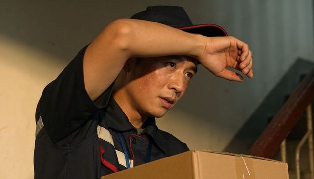 Delivery courier sweating and wiping forehead while carrying parcel on stair landing