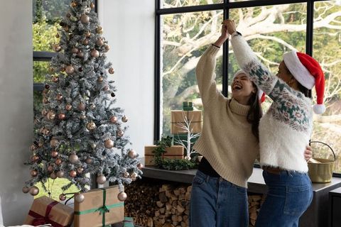 Friends dancing beside flocked christmas tree with wrapped gifts and santa hat