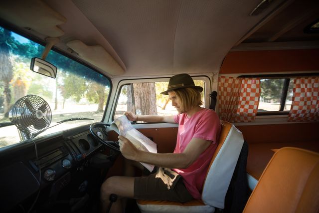 Side view of man reading map while sitting in camper van