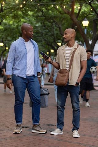 Two african men walking and talking on brick promenade at dusk carrying cooler and phone