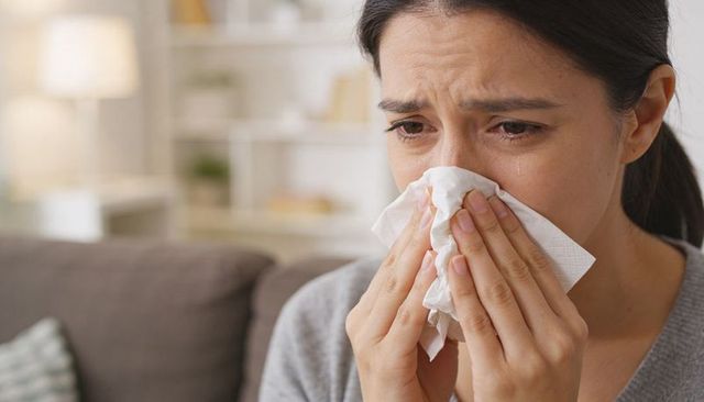 Woman crying and wiping nose with tissue on couch at home closeup emotional portrait