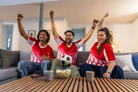 Multicultural friends cheering and celebrating soccer match while watching game at home