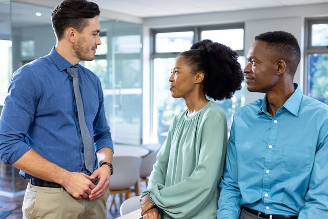 Diverse group of colleagues engaging in a discussion in a modern office environment. Ideal for use in business and corporate materials, presentations, teamwork and collaboration themes, and professional communication contexts.