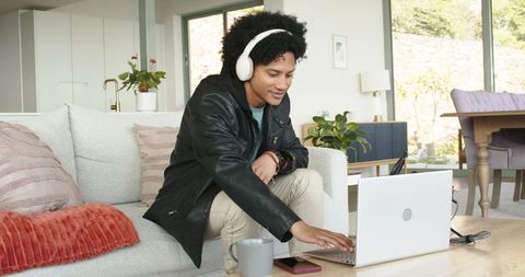 African american man working from home wearing headphones and leather jacket on sofa