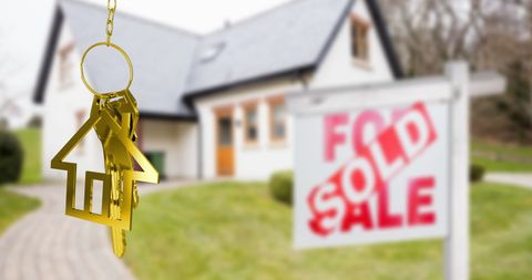 Golden house key fob in front of sold property sign