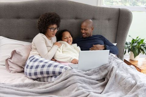African american family cuddling in bed watching laptop, cozy morning together