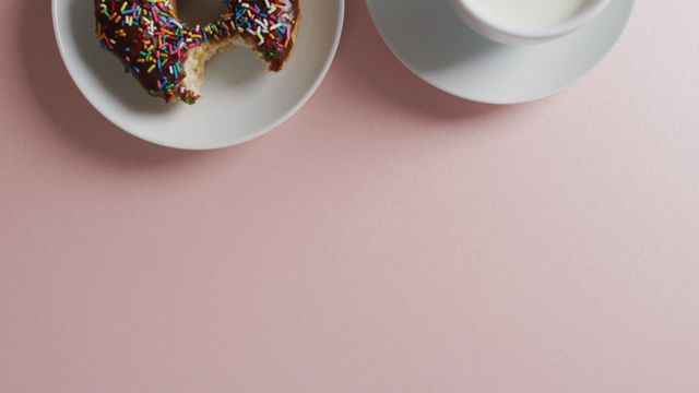 A vibrant, mouth-watering video of a chocolate frosted donut with colorful sprinkles and a cup of milk on a pink background. Perfect for use in food blogs, dessert menus, café promotions, breakfast advertising, and social media posts celebrating fun and tasty treats.