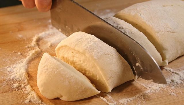 Slicing Rolled Dough Log into Even Portions on Wooden Cutting Board with Chef Knife