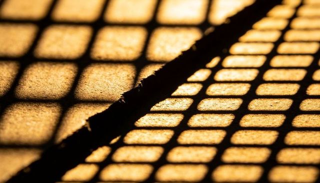 Frayed rope crossing sunlit metal grate casting golden grid shadows and textured contrast