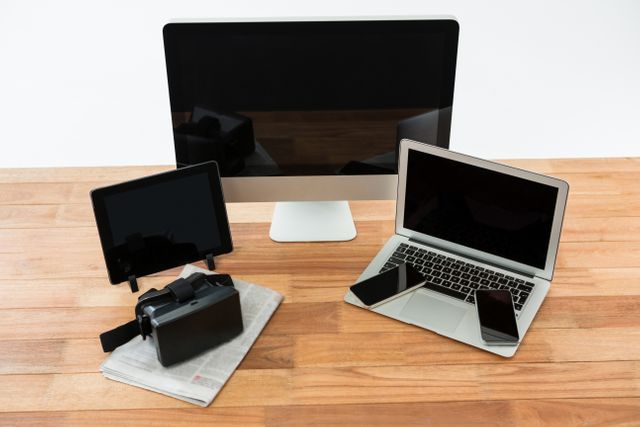 Computer, laptop, digital tablet, mobile phone, virtual headset and newspaper on wooden table