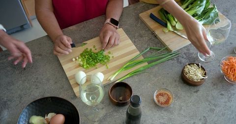 Multigenerational women chopping green onions with wine on kitchen countertop